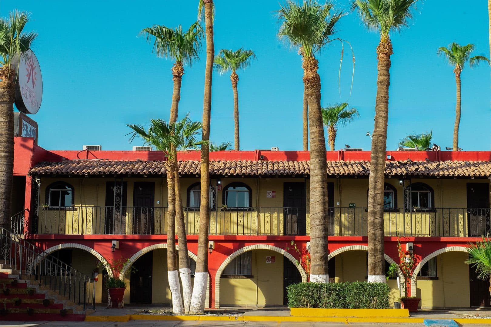 Fachada estilo hacienda con arcos rojos, balcones y palmeras